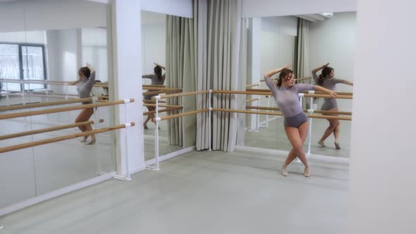 The girl dances a modern dance in a bright studio with mirrors. Slow motion, smooth motion.