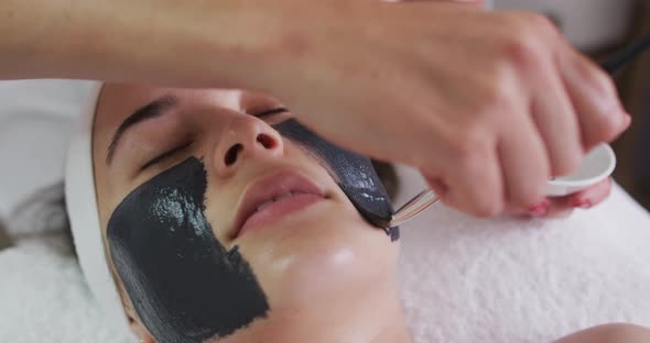 Caucasian woman lying back while beautician gives her a face mask