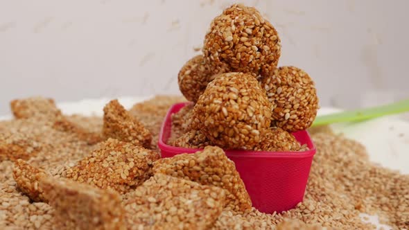 Plastic bowl filled with sesame seed ladoos and sprinkling of sesame seeds