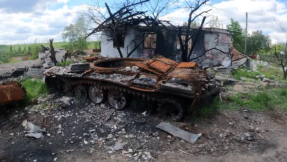 Burnt Russian Tank Against the Backdrop of a House Destroyed By Shelling