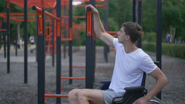 Brunette Caucasian Young Man Standing Up From Wheelchair Holding Gymnastic Set Outdoors in Park