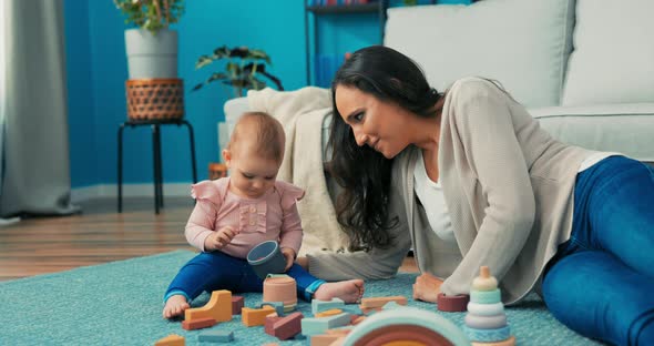 Funny Cute Girl is Playing with Blocks with Mother on Carpet She Takes Plastic Container