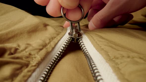 A Man Fastens a Metal Zipper on a Beige Jacket in Macro