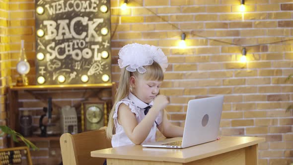 Little Girl Sits at Table and and Typing on the Laptop Keyboard on the Background of a School Class