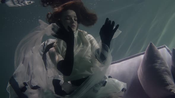 a Woman in a Long Dress Poses Beautifully on a Gray Sofa with Pillows Which Is Under Water