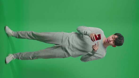 Full Body Of Asian Man Enjoy Using Mobile Phone While Standing On Green Screen In The Studio