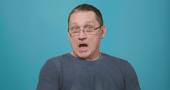 Man in Glasses and Grey T-shirt Sneezes Into Upper Sleeve
