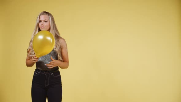 Female Model in Silver Tank Top Holding a Ballon Against a Yellow Background