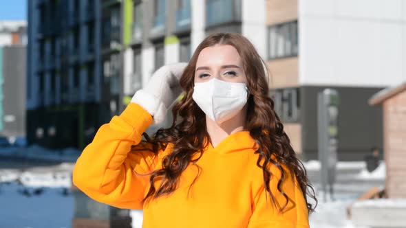 Beautiful Girl Portrait in a Protective Mask and a Yellow Sweatshirt Outdoors on a Winter