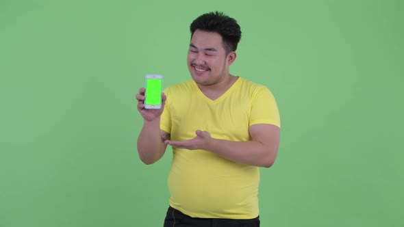 Happy Young Overweight Asian Man Showing Phone and Giving Thumbs Up