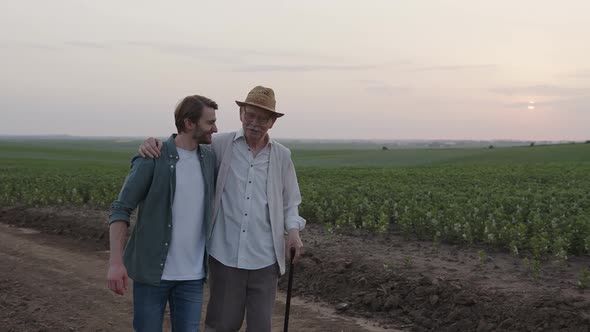 Two Farmers Walk and Hug on the Road Near Their Field