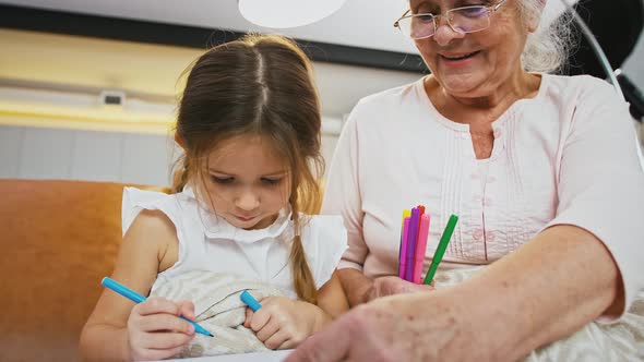 Aged Grandma and Little Grandchild are Talking and Smiling Drawing with Felttip Pens on a Sheet of