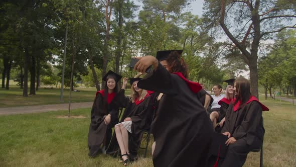 Group of Joyful Diverse Multiethnic Graduates Recording Video on Phone at Graduation Day