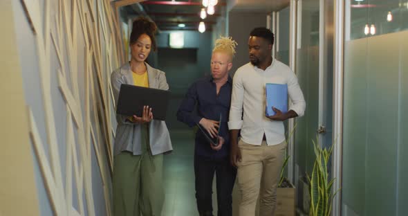 Diverse business people discussing with laptop and walking in creative office