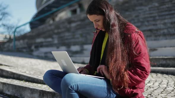 Focused Mature Woman with Long Dark Hair Using Laptop Outdoor