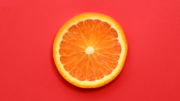 Slice of orange rotating top view on red background