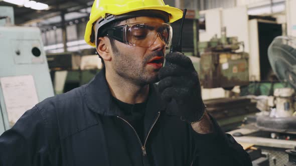 Factory Worker Talking on Portable Radio While Inspecting Machinery Parts