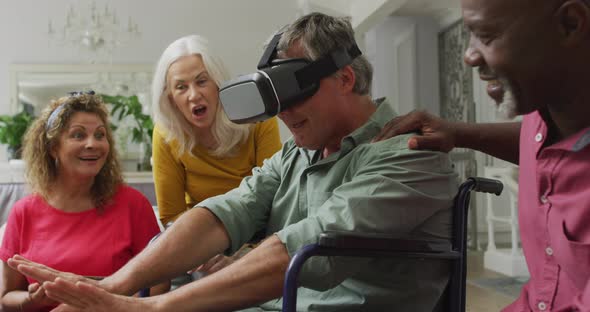 Video of happy senior man in wheelchair using vr headset and having fun with diverse friends