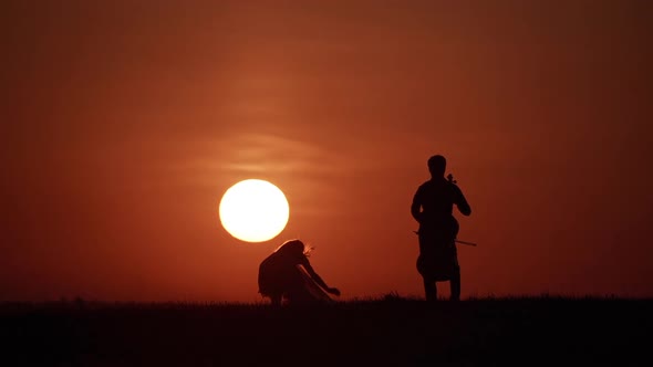 Silhouette of Woman Dancer and Cellist Opposite Big Sun in Sky