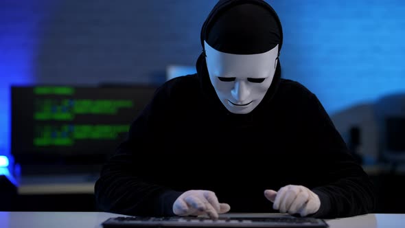 Concentrated Hacker Typing on Keyboard Raising Masked Face and Pointing at Camera