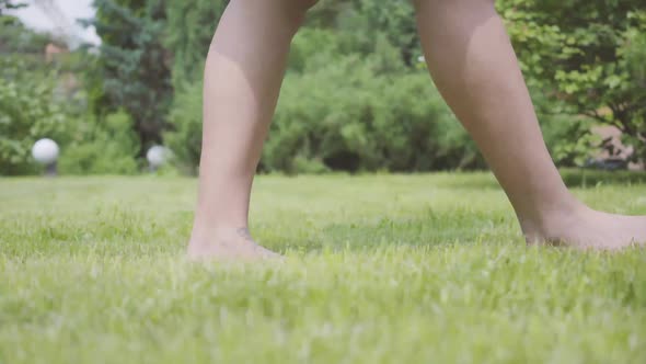 Legs of the Young Woman Walking on the Grass Barefoot in the Garden