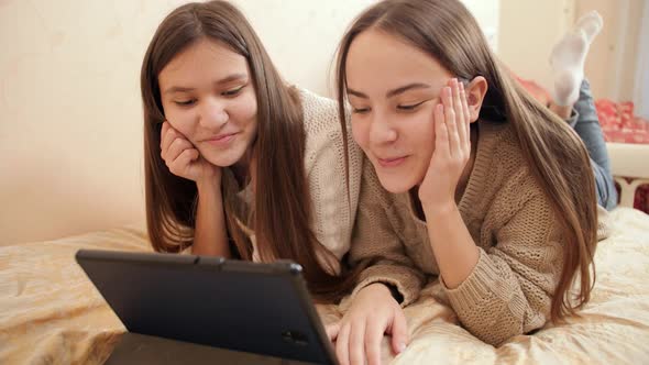 Portrait of Two Smiling Teenage Girls Having Video Conference on Tablet Computer While Lying on Bed