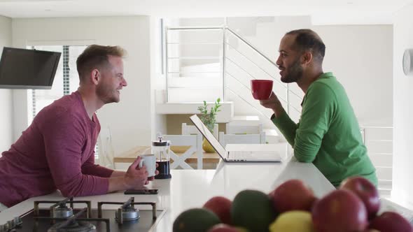 Multi ethnic gay male couple drinking coffee talking in kitchen