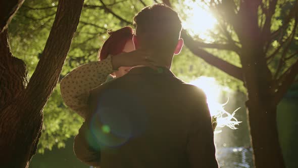 Unrecognizable Couple of Man and Woman Hugging Under Tree and Kissing Against Backdrop of Setting