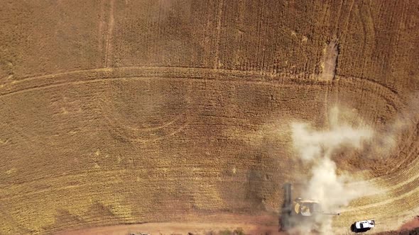 Straight down aerial view of a combine harvesting crops and spreading dust up into the sky