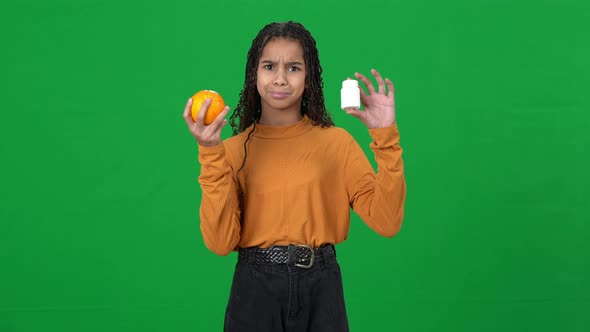 Unsure African American Teen Girl on Green Screen Holding Drugs and Orange Shrugging Shoulders