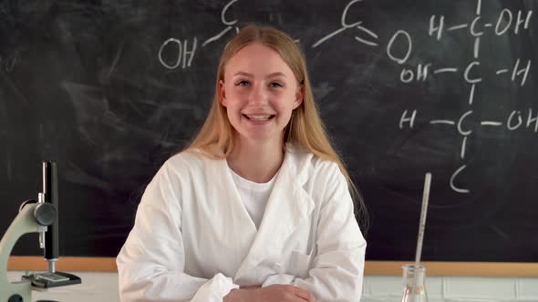 Online Chemistry Lesson and Teacher Young Millennial Woman in White Medical Coat Sitting at a Desk