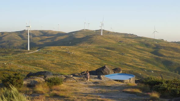 Woman in Casa do Penedo Boulder House swimming pool with view to wind turbines landscape in Fafe, Po