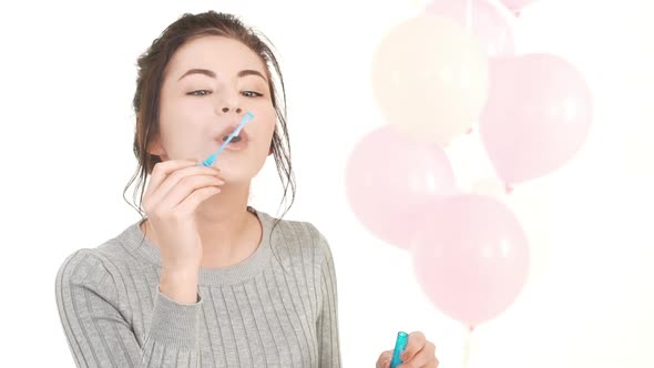 Beautiful Young Caucasian Girl with Brunette Hair Blowing Soap Bubbles and Smiling Standing on White