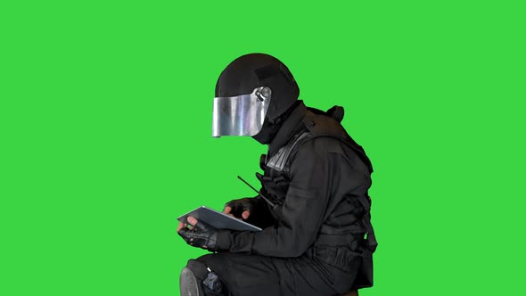 SWAT Team Officer Sitting and Using Digital Tablet on a Green Screen Chroma Key