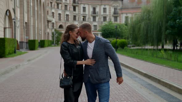 Happy Loving Man and Woman are Walking in Rain in Daytime Embracing Each Other