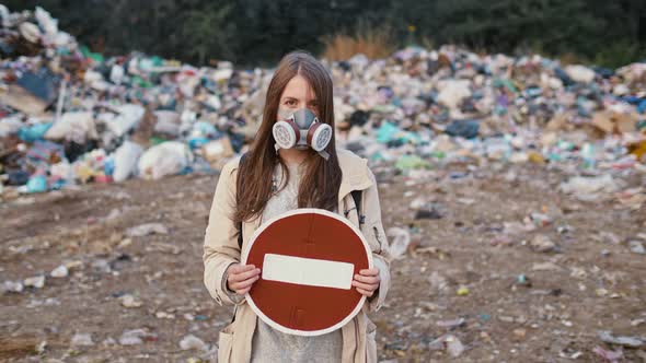 Portrait of Sad Young Woman in Gas Mask Holding Stop Sign While Standing in Toxic Smoke