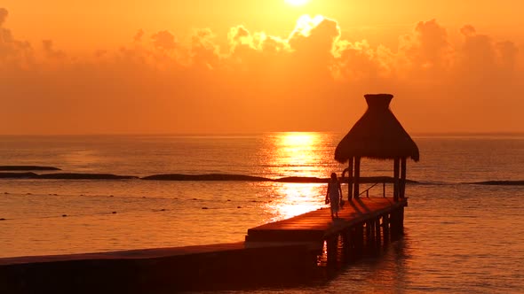 Woman walks along dock during sunset at tropical resort