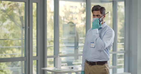 Male Security in Safety Gloves and Mask Talk on Walkietalkie Standing Near Entrance