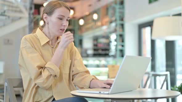 Coughing Young Woman Using Laptop in Cafe