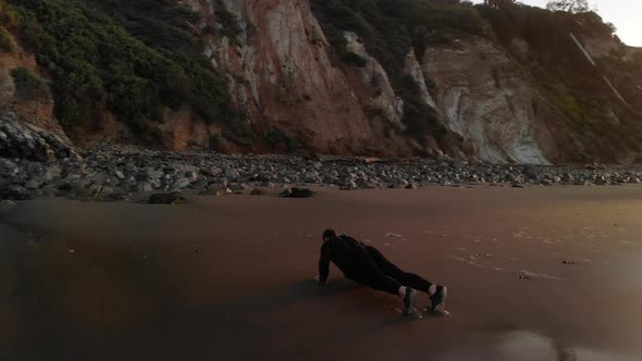 A strong muscular man doing push ups for a morning fitness workout at sunrise on a beach in Santa Ba