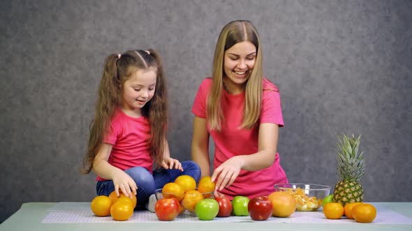 Happy little girl and her mother with fruits at home. 