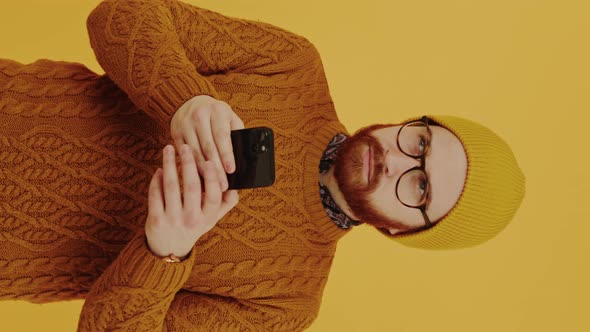 Vertical Studio Shot of a Bearded European Young Adult Guy in a Beanie and Knitted Sweater Using His