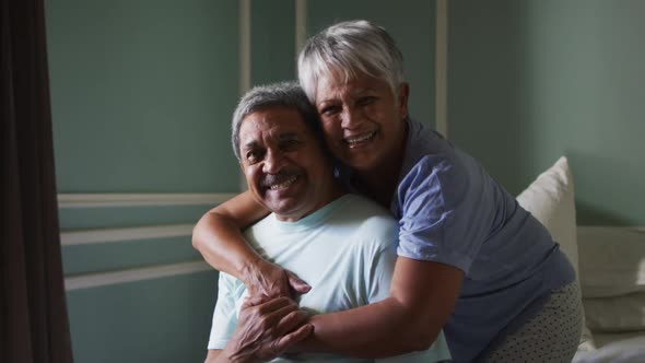 Senior mixed race couple embracing and laughing in bedroom