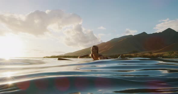 Beautiful woman paddling out to surf at sunset alt