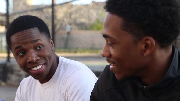 Two young basketball players talking on the sidelines of a street court.