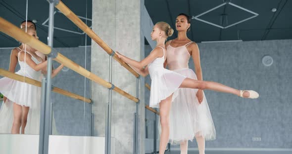 Woman Helps Little Ballerina Do Raise Up Leg Near Barre