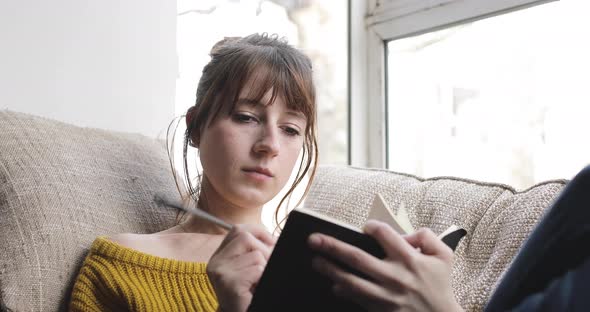 Woman sitting on couch and writing into a book