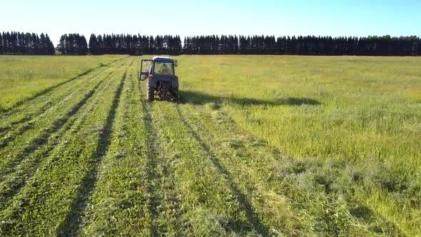 Flycam Follows Tractor Mowing Grass Shining in Sun Rays