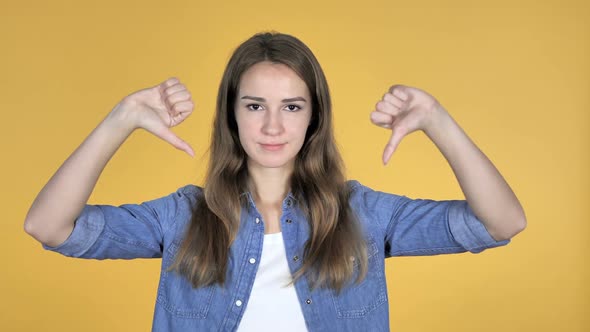 Pretty Woman Gesturing Thumbs Down Isolated on Yellow Background