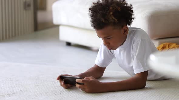 African American Boy is Using Smartphone While Lying on Floor at Apartment Room Spbi